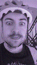 a selfie of a white person, wearing either headphones or a helmet, making an odd expression. the photo is edited to be colorized into a monochrome purple-ish color palette.